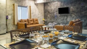 Una sala de estar moderna con un sofá, sillas, una mesa de comedor para cuatro personas y un televisor de pantalla plana en la pared.