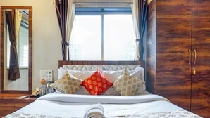 Habitación de hotel con una cama grande, un armario de madera, una ventana con cortinas y un espejo.