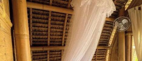 Una habitación con cama, mosquitera y ventilador.