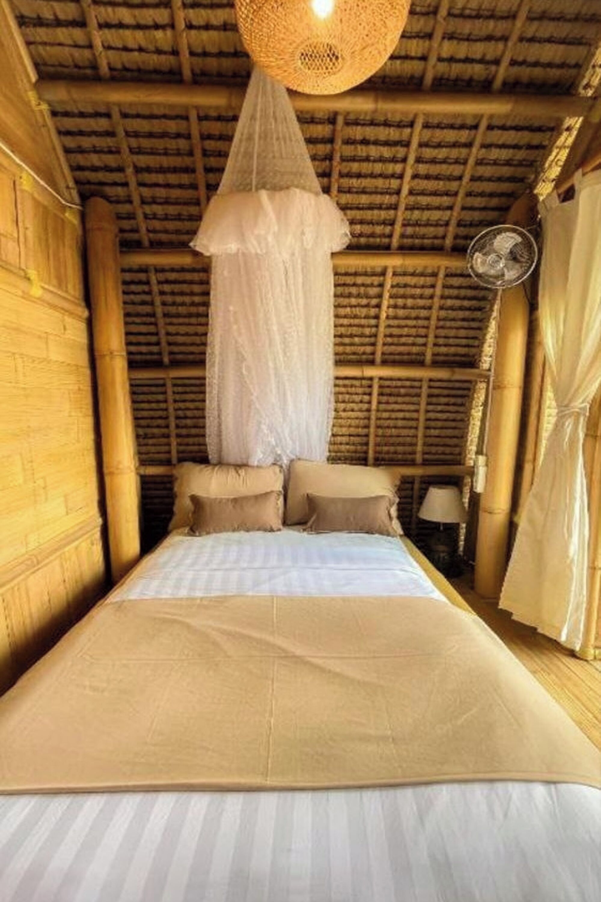 Ein Zimmer mit einem Bett, einem moskitoschutzenden Moskitonetz und einem Deckenventilator.