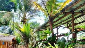 A tropical garden with a pond, palm trees, and a thatched-roof structure. - Tiny ECO Bamboo Ubud (Sebatu)