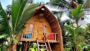 A wooden house with a thatched roof, surrounded by lush greenery and palm trees. - Tiny ECO Bamboo Ubud (Sebatu)