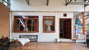 Una habitación con suelo de baldosas, bancos de madera, una mesa cubierta con tela y ventanas grandes con cortinas.