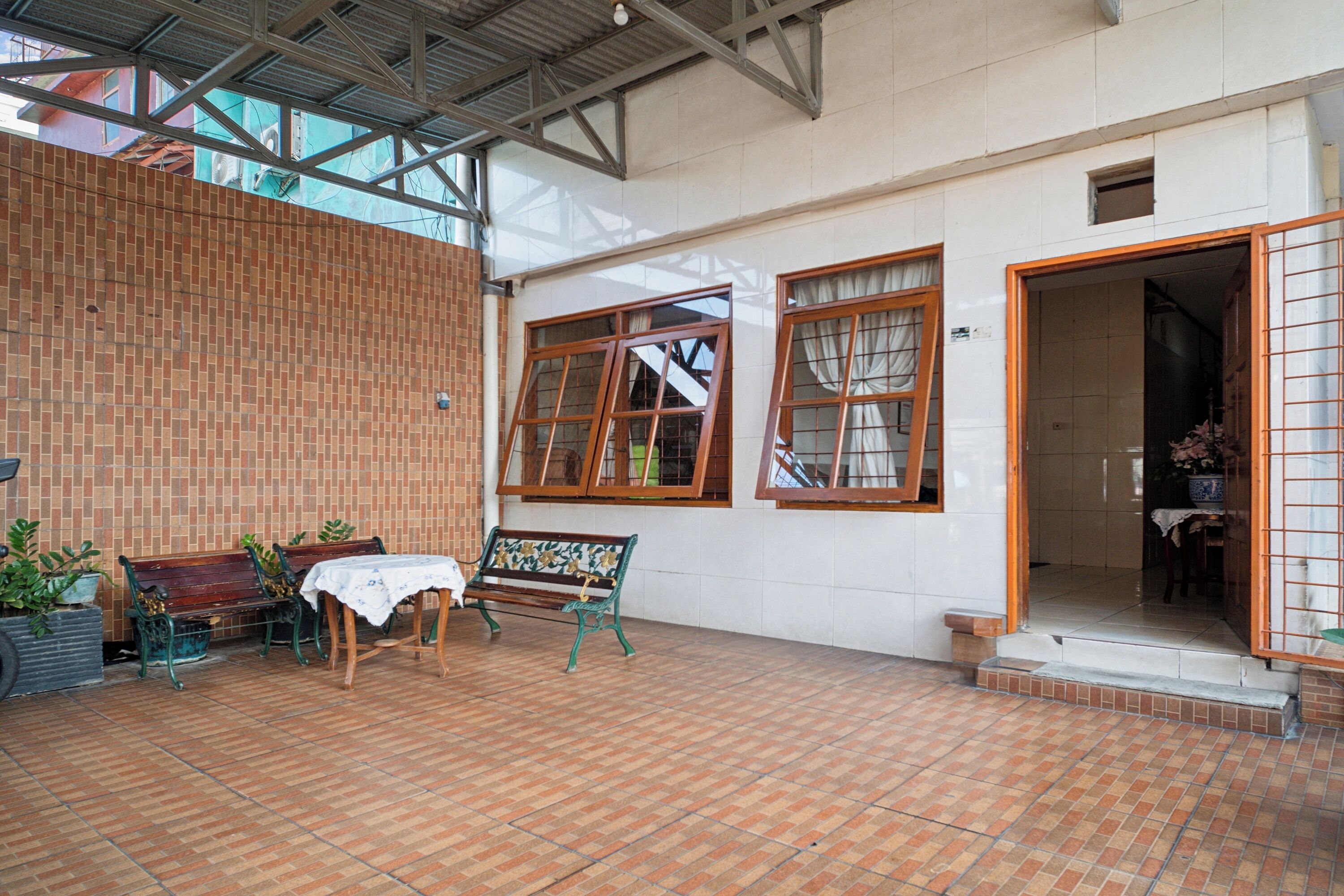 A covered patio area with brick flooring, wooden benches, and potted plants.