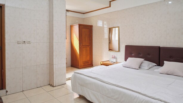 Habitación de hotel con una cama grande, un armario de madera, una mesita de noche y un espejo en la pared.