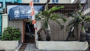 Un edificio con un cartel publicitario de una propiedad en venta, una palmera y un pequeño jardín.