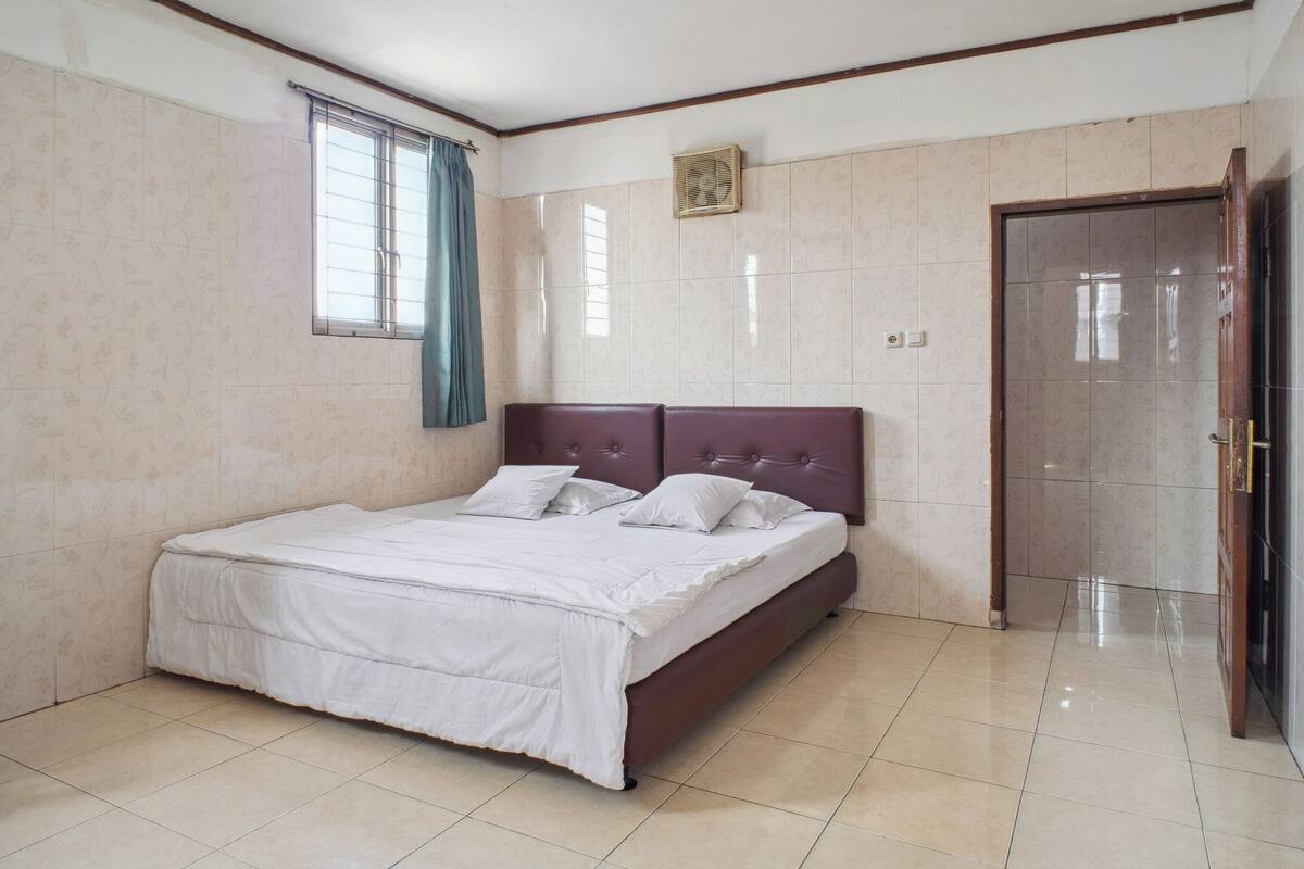 A bedroom with a bed, a window with curtains, a door, and a fan on the wall.