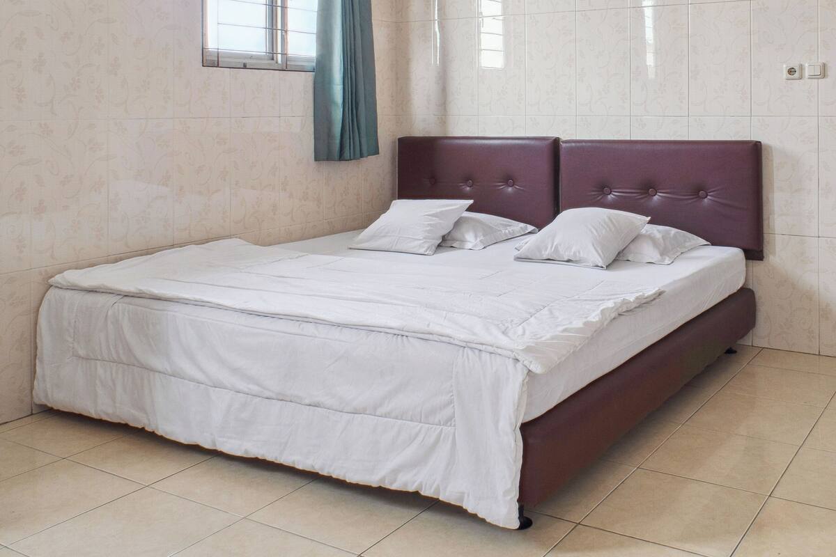 A neatly made bed with a headboard, white bedding, and a window with curtains.