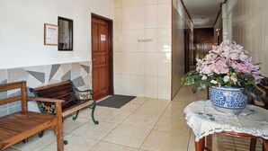 Un área de recepción con un banco de madera, una planta en maceta y piso de baldosas.