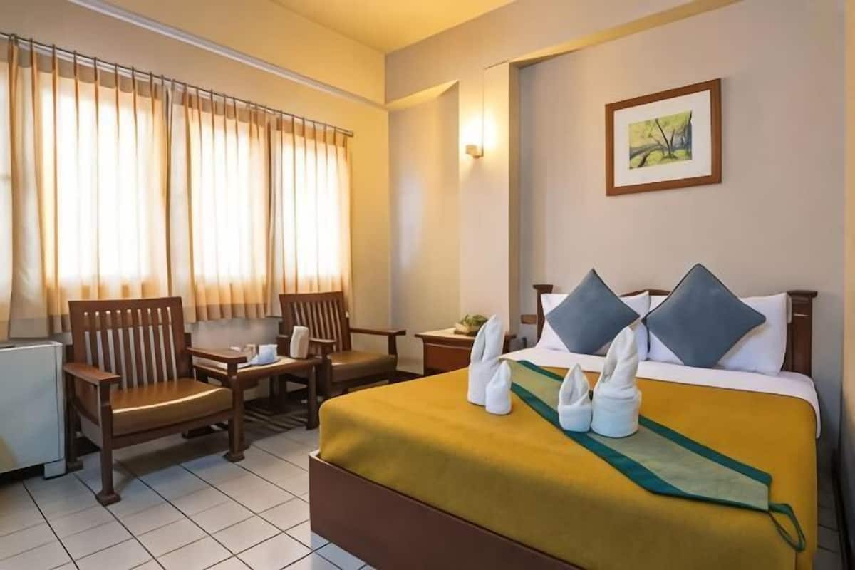 Une chambre d’hôtel avec un lit, deux chaises, une petite table, une lampe et un tableau au mur.