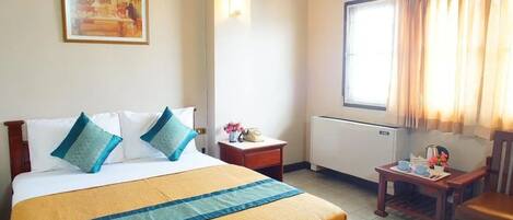 Hotellihuone, jossa on sänky, pieni pöytä teekupit ja -lautaset valmiina, tuoli, ikkuna, jossa on verhot, ja taulu seinällä.