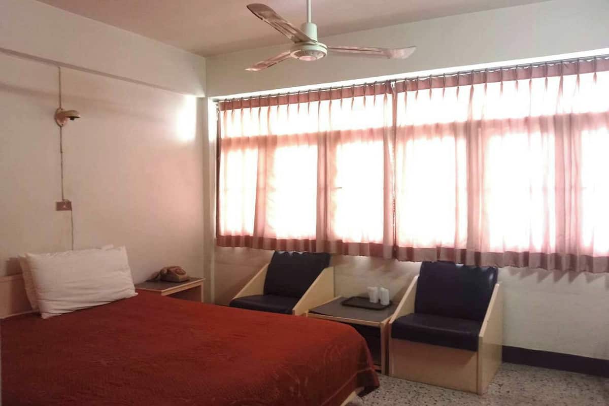 Une chambre d’hôtel avec un lit, deux chaises, une petite table et un ventilateur de plafond.