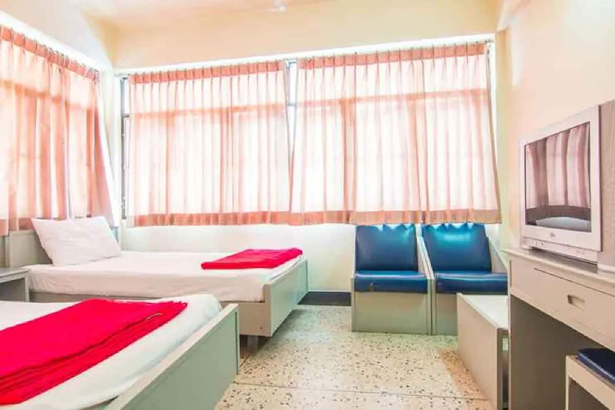 Une chambre d’hôtel avec deux lits, une télévision, un bureau et une fenêtre avec des rideaux.