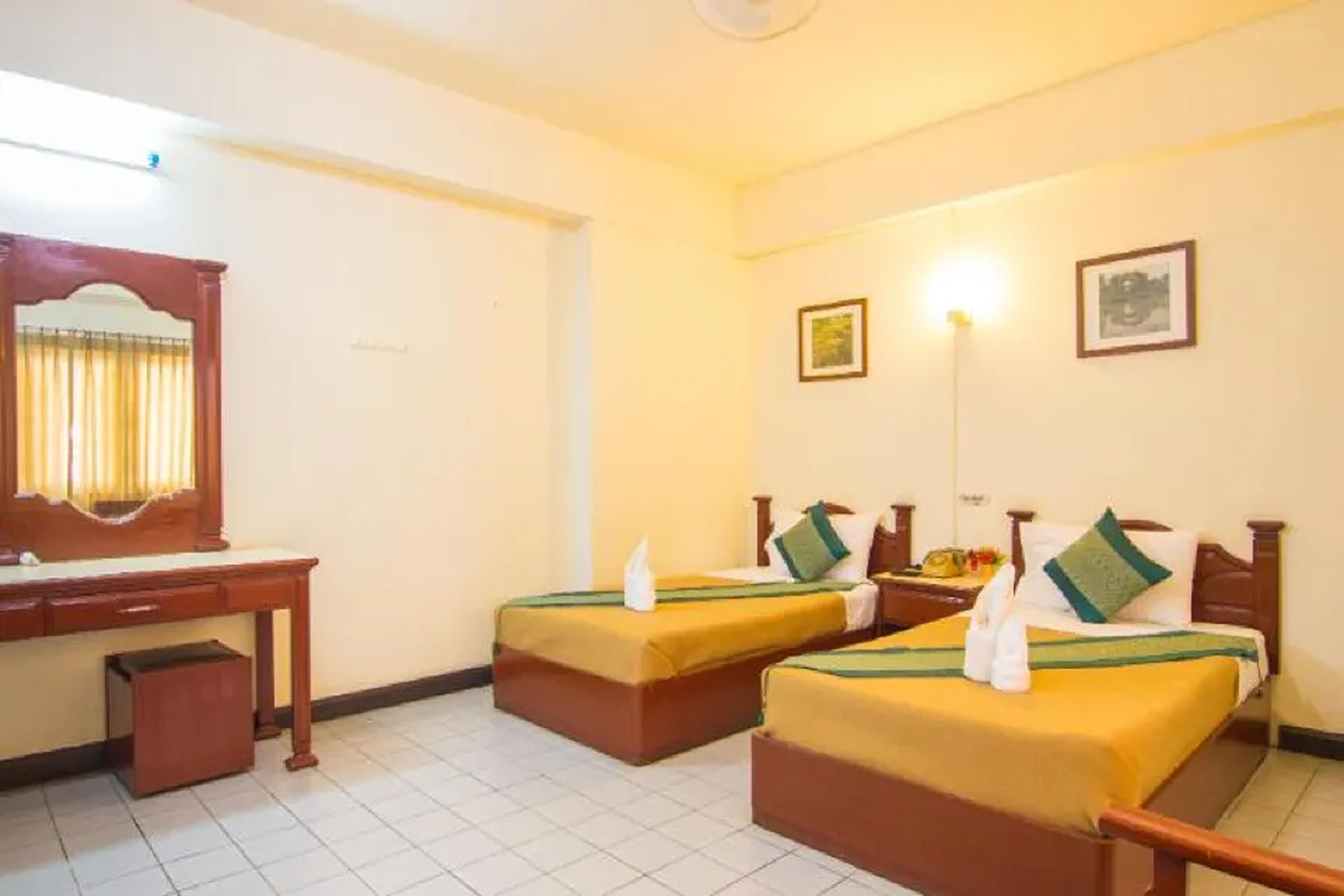 A hotel room with two single beds, a wooden desk, a mirror, and a small trash bin.