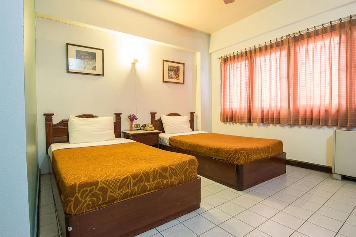 Une chambre d’hôtel avec deux lits simples, une table de chevet avec une lampe et une fenêtre avec des rideaux.