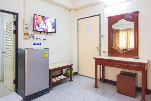 A compact hotel room with a refrigerator, a television mounted on the wall, a wooden desk, and a mirror above it. - Khelang Nakorn Hotel (Lampang)