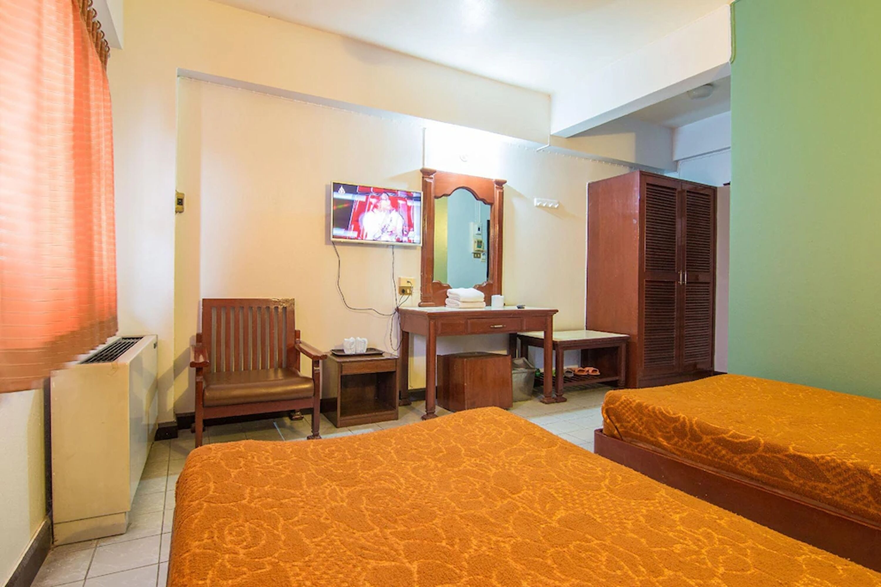 A hotel room with two beds, a wooden desk, a chair, a television, and a wardrobe.