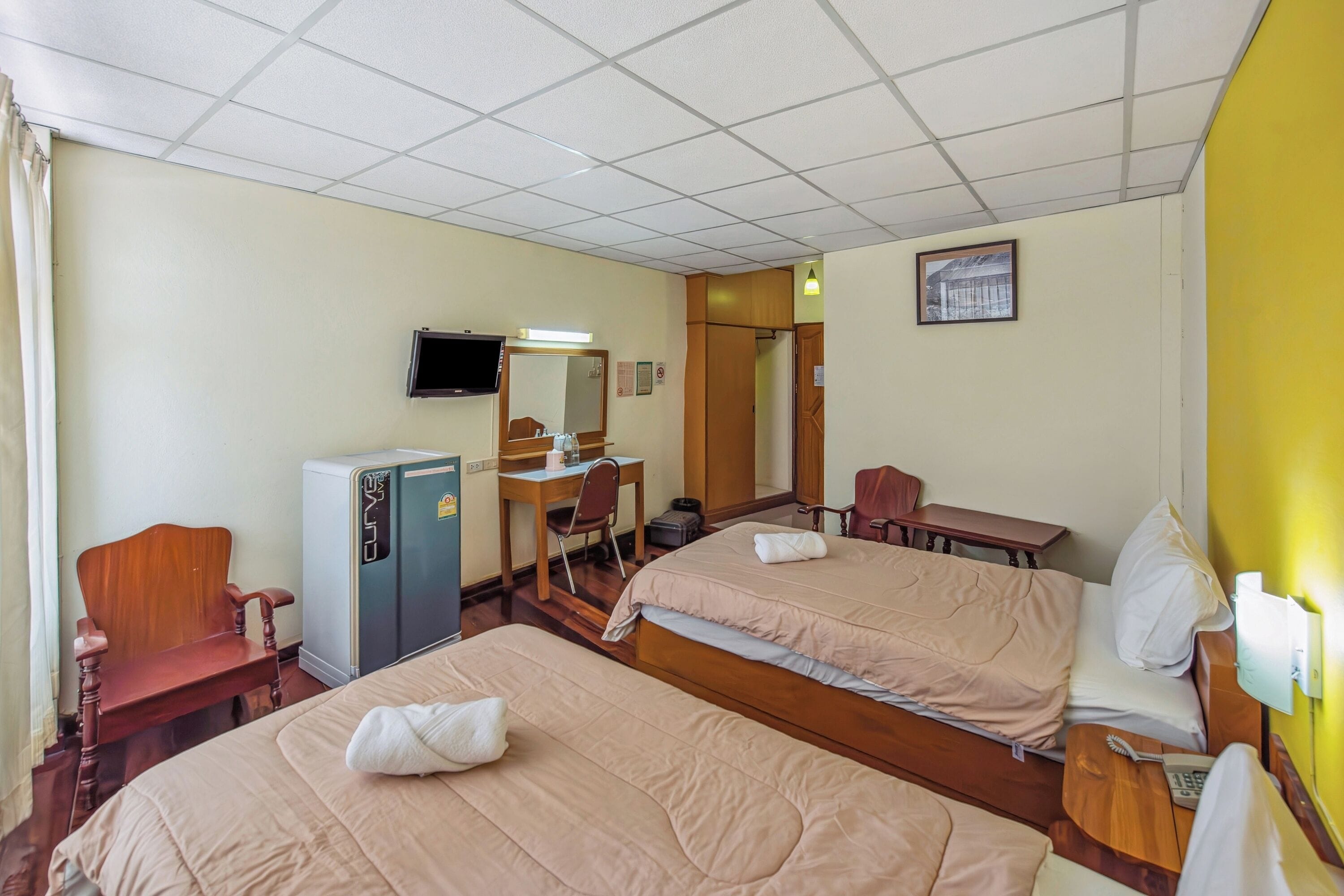 Ein Hotelzimmer mit zwei Betten, einem Schreibtisch, einem Sessel, einem Fernseher und einem Kleiderschrank.