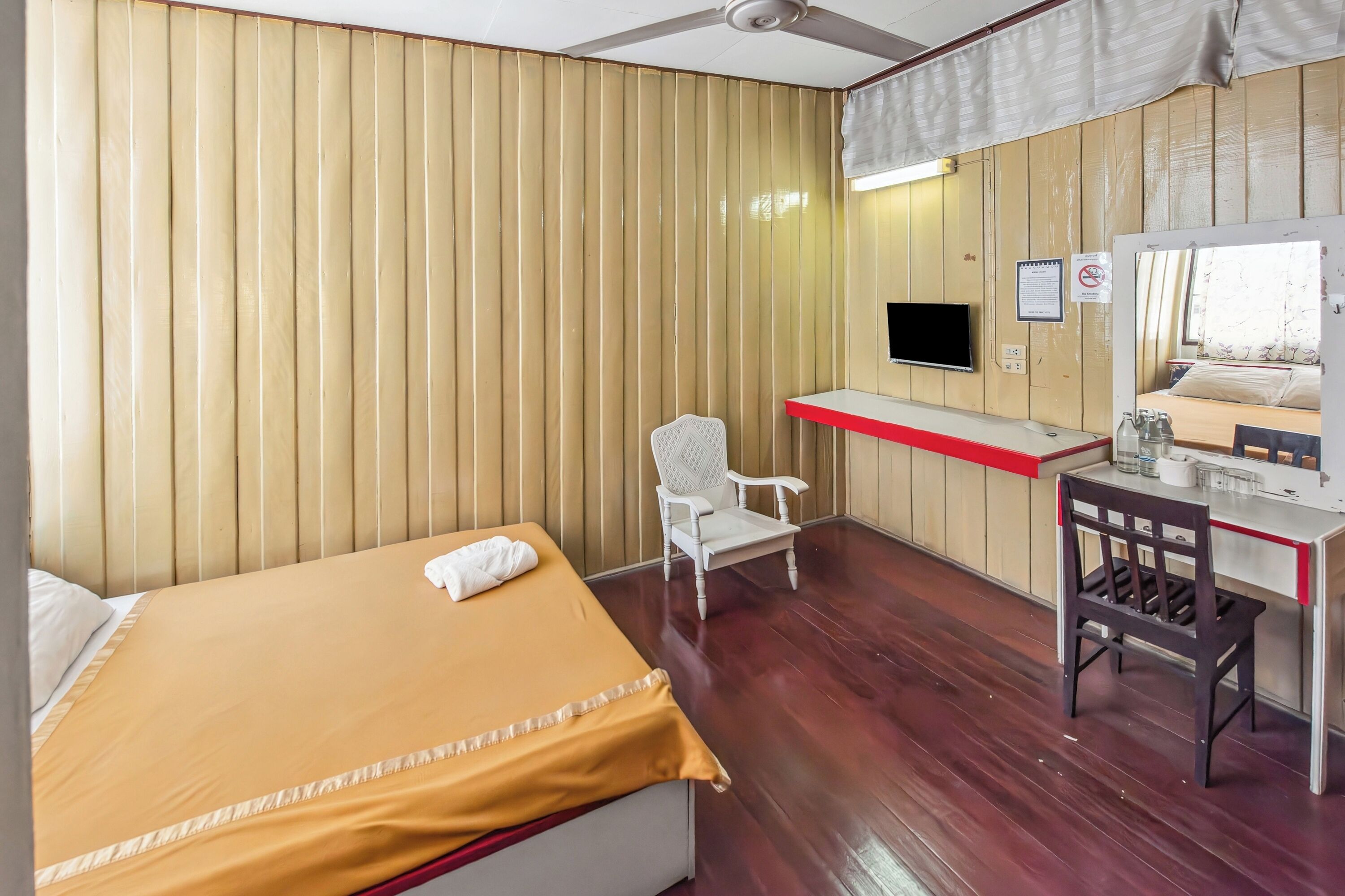 A hotel room with a bed, a desk, a chair, a television, and a mirror.