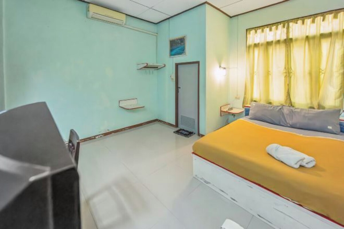 Quarto de hotel com cama, escrivaninha, cadeira, janela com cortinas e porta.