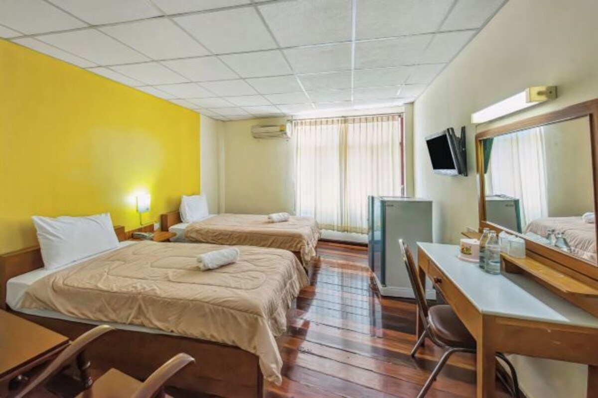 Quarto de hotel com duas camas, uma escrivaninha, uma cadeira, uma televisão e uma janela com cortinas.
