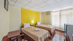 A hotel room with two beds, a desk, a chair, and a window with curtains. - The Prince Hotel (Phitsanulok)
