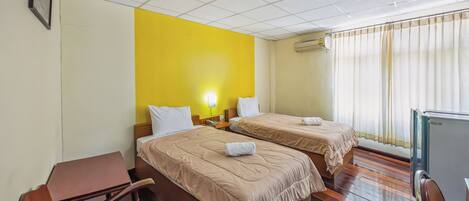 Habitación de hotel con dos camas, un escritorio, una silla y una ventana con cortinas.
