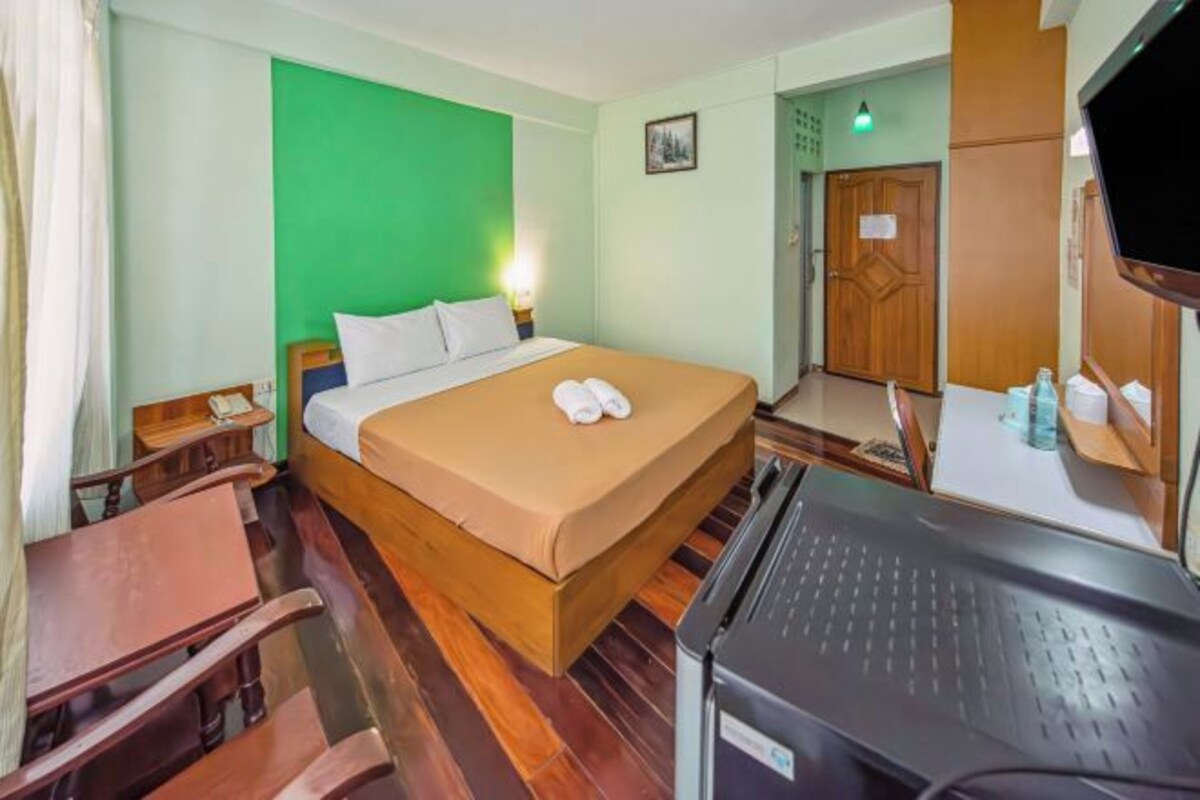 Quarto de hotel com cama, escrivaninha, cadeira, televisão e parede verde.