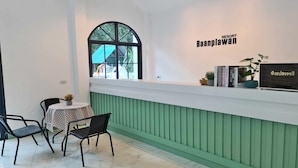 A reception area with a checkered table, black chairs, a green wall, and a large window. - Baan Plawan Resort Chiang Rai (Chiang Rai)