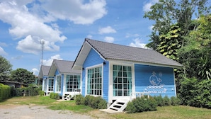 A row of blue seaside cottages with large windows, a grassy front yard, and a clear sky. - Baan Plawan Resort Chiang Rai (Chiang Rai)