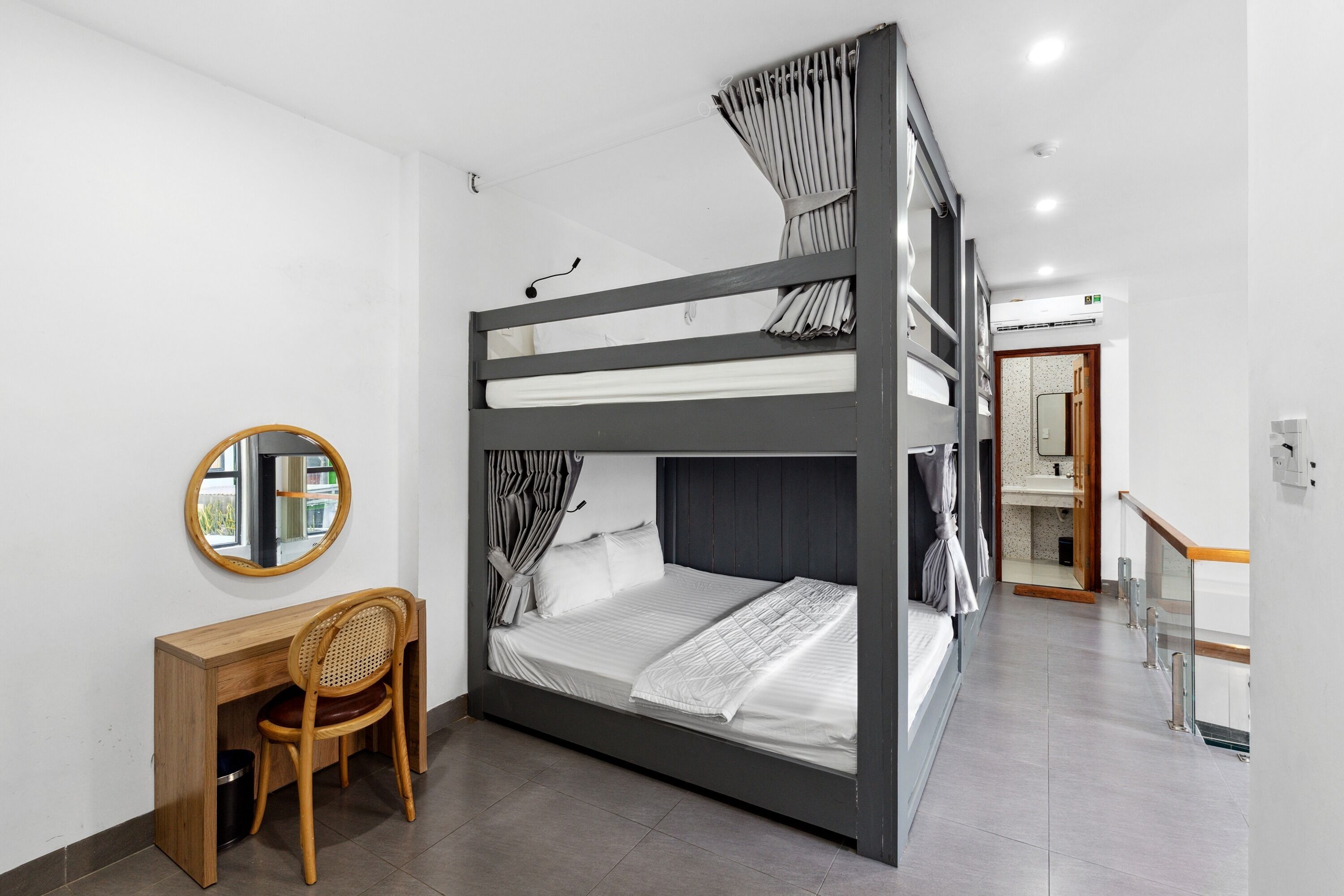 A bunk bed room with a desk and chair, a round mirror, and a bathroom visible in the background.