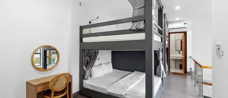 A bunk bed room with a desk and chair, a round mirror, and a bathroom visible in the background.