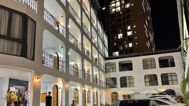 A multi-story hotel with a courtyard, featuring balconies, outdoor seating, and a Mercedes-Benz parked in the foreground. - Mai Hotel (Ho Chi Minh City)