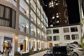 A multi-story hotel with a courtyard, featuring balconies, outdoor seating, and a Mercedes-Benz parked in the foreground. - Mai Hotel (Ho Chi Minh City)