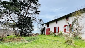 Un bâtiment blanc avec des volets rouges et un grand arbre devant.