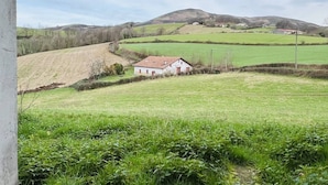 Un paysage rural avec des collines ondoyantes, un bâtiment blanc avec un toit rouge et des champs verdoyants.