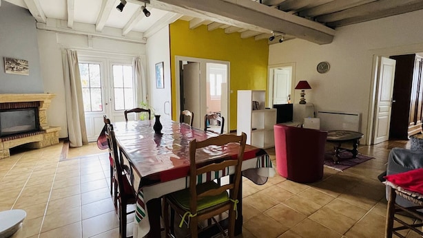 Un vaste espace de vie comprenant une grande table à manger en bois, une cheminée et un mur d’accent jaune.