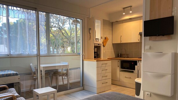 Een compact studio-appartement met kitchenette, eethoek en bed met een kleurrijk dekbed.