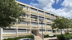 Een meerlaags appartementencomplex met een centrale ingang, een auto ervoor en omliggend groen.