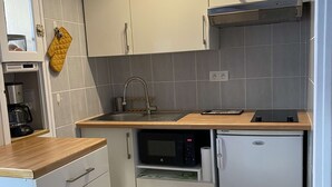 Een compacte keuken met een ingebouwde magnetron, een kleine koelkast en een spoelbak met een houten aanrecht.
