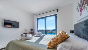 Een moderne hotelkamer met een groot bed, een flatscreen televisie, uitzicht op zee en een balkon met een schuifdeur.