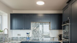 A modern kitchen with dark cabinetry, a marble backsplash, and stainless steel appliances.