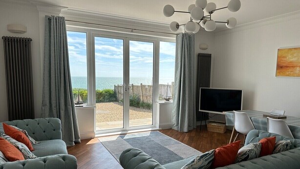 A spacious living room with a large sliding glass door leading to a balcony, a flat-screen TV, and a dining area with chairs.