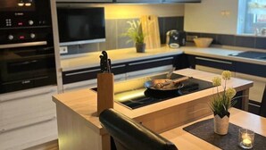 Una cocina moderna con una isla central, horno integrado y un área de comedor con una silla y una mesa.