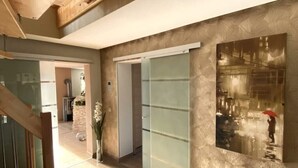 Un interior moderno con una puerta de vidrio que da a una cocina, una escalera y una obra de arte enmarcada en la pared.