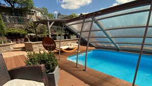 Zona de piscina con cerramiento de vidrio, mobiliario de mimbre y un letrero que dice "Auszeit".
