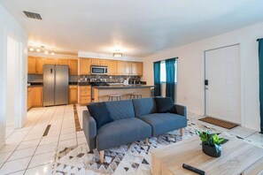 A modern living room with a grey sofa, a coffee table with a plant, and a kitchen in the background. - 505 Fillmore Uint 12 | 1BR/1BA (Cape Canaveral)