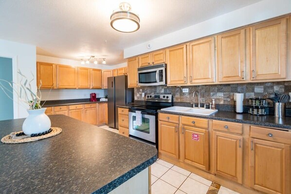 A modern kitchen with wooden cabinets, a granite countertop, stainless steel appliances, and a backsplash.