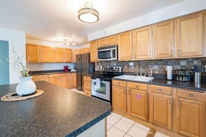 A modern kitchen with wooden cabinets, a granite countertop, stainless steel appliances, and a backsplash.