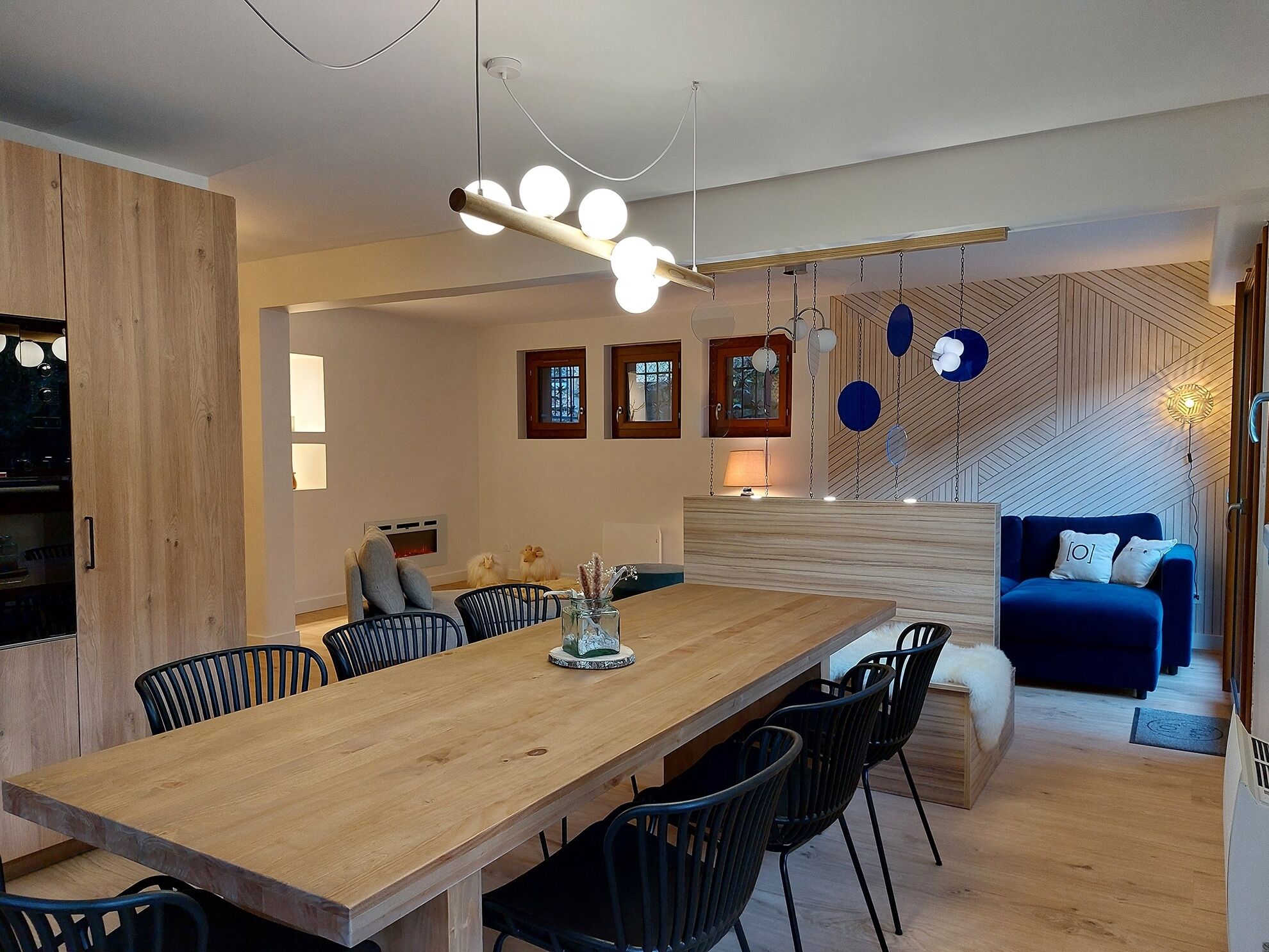 A modern kitchen with a wooden dining table and chairs, a built-in oven, and a hanging light fixture.